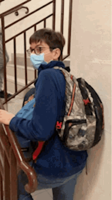 a young boy wearing a mask and a backpack climbs a set of stairs