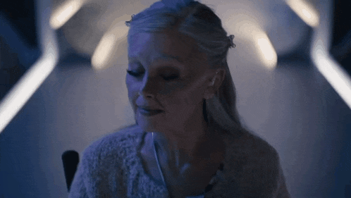a woman with white hair is sitting in a chair in a dark room with a blue light behind her .