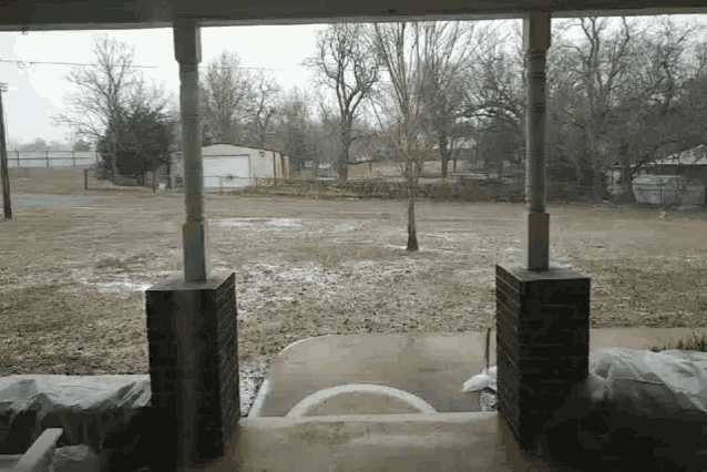 a porch with a view of a field with trees and a garage in the background
