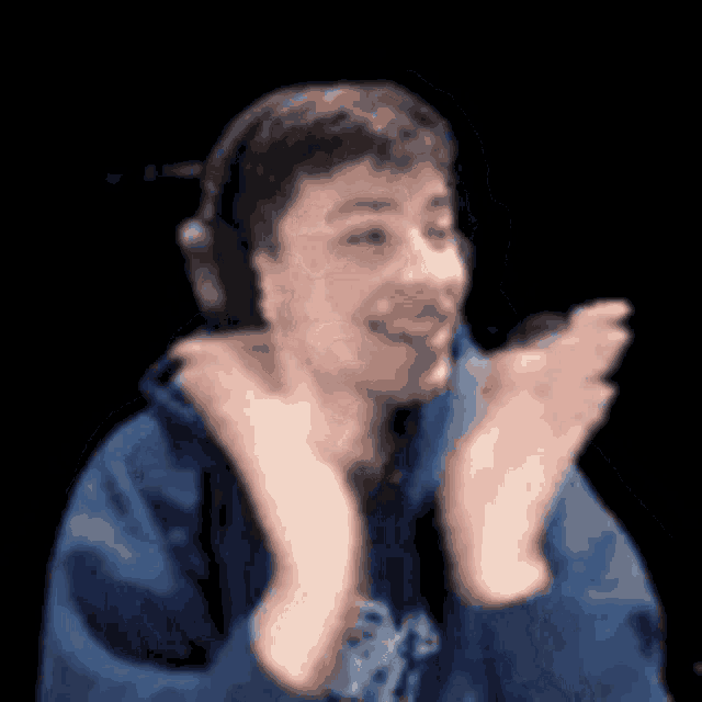 a young man wearing headphones and a blue hoodie is clapping his hands .