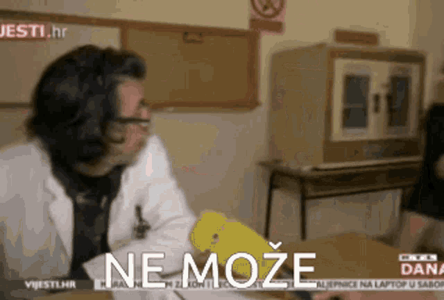 a man in a lab coat is sitting at a table with a yellow object and the words ne moze on the screen