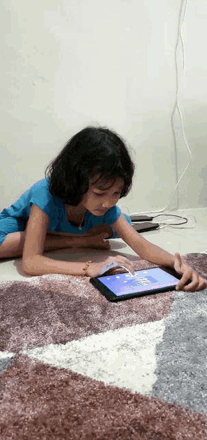 a little girl is laying on the floor playing on a tablet