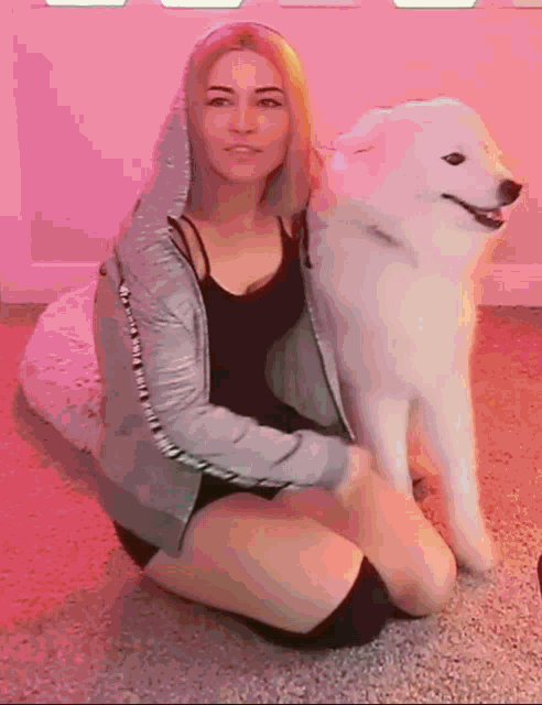 a woman is kneeling down next to a white dog with a pink background