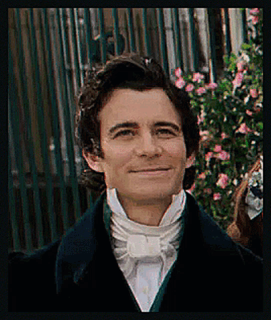 a man in a suit and tie is smiling in front of some flowers