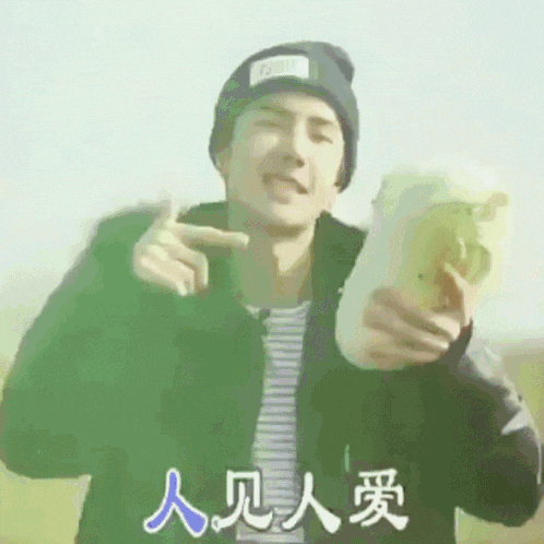 a man wearing a black beanie and a black jacket is holding a sandwich and pointing