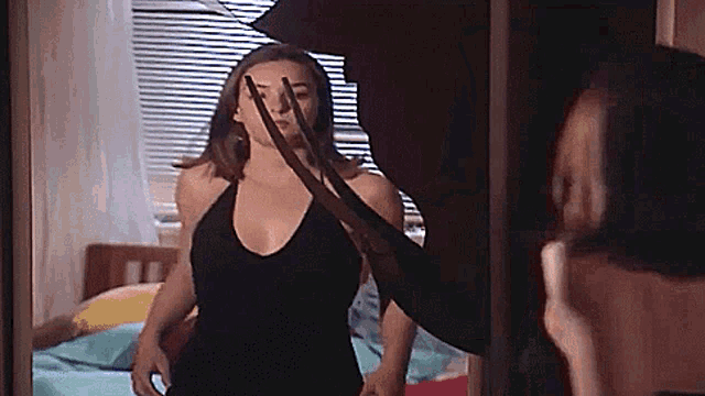 a woman in a black dress is standing in front of a mirror holding a sword .