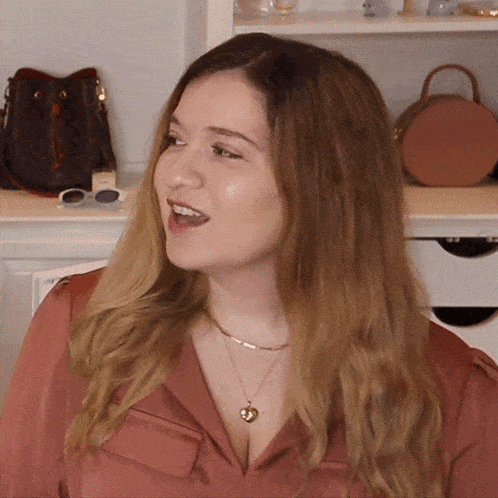 a woman wearing a heart shaped necklace stands in front of a louis vuitton purse
