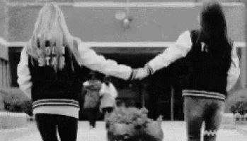 two girls are holding hands while walking down a sidewalk in front of a building .