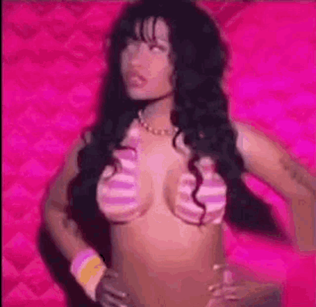 a woman is standing in front of a pink wall wearing a bikini top .