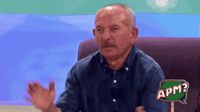a man with a mustache is sitting in front of a sign that says apm