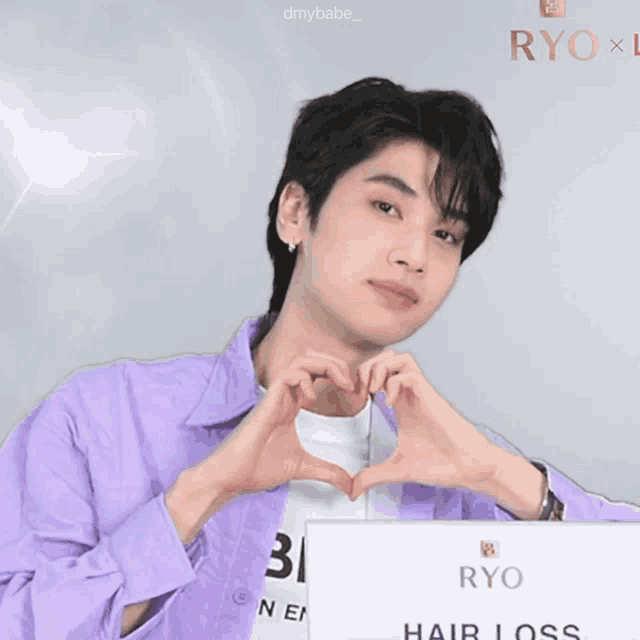a man in a purple shirt making a heart with his hands