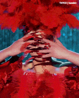 a woman with long red nails and a red feathered headpiece covering her face