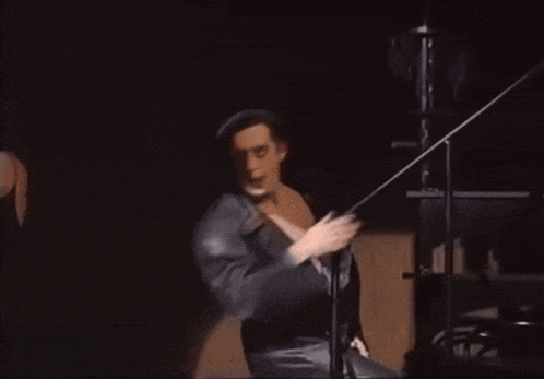 a man in a black robe is dancing on a stage in front of a microphone