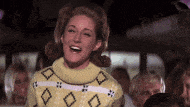 a woman wearing a yellow sweater with diamonds on it is laughing
