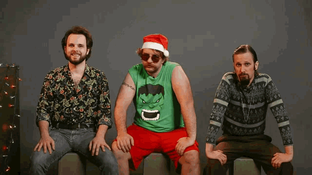 a man wearing a santa hat and a hulk shirt sits with two other men