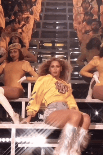 a woman wearing a yellow sweatshirt that says ' beyonce ' on it is sitting on a stage