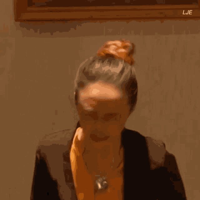 a woman in a suit and orange shirt is standing in front of a framed painting .