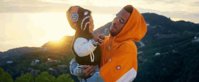 a man is holding a baby in his arms in front of a mountain .