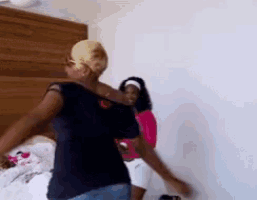 two women are dancing in a room with a wooden headboard in the background .
