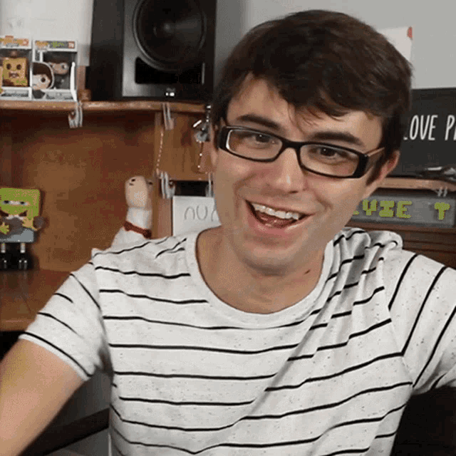 a man wearing glasses and a striped shirt smiles in front of a sign that says " love people "