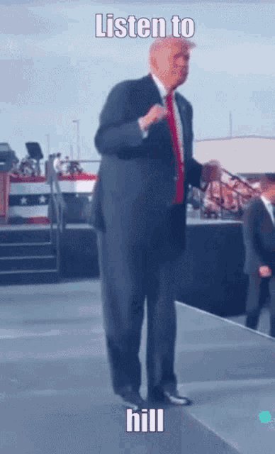 a man in a suit and tie is standing on a stage with the words listen to hill below him