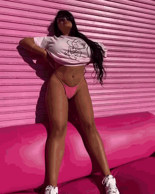 a woman laying on a pink couch in front of a pink wall wearing a t-shirt with a face on it