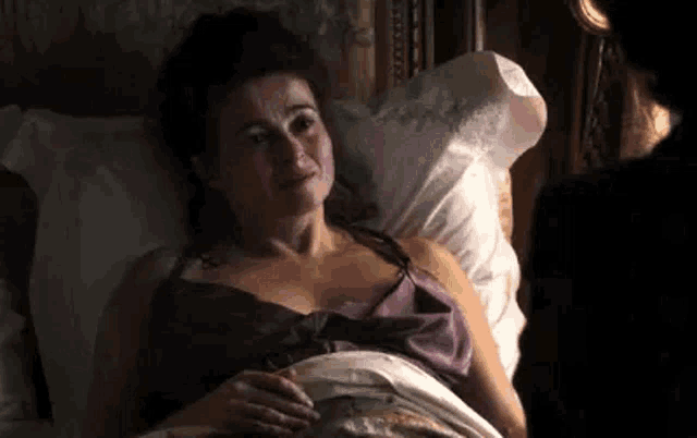 a woman in a purple dress is laying in bed talking to a man .