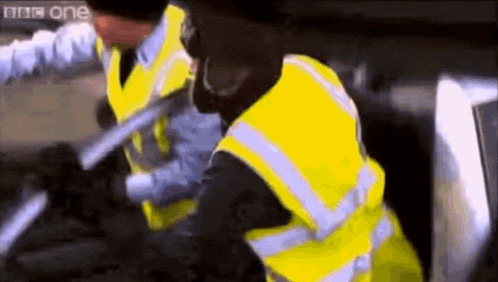 two men wearing yellow vests are fighting with a bbc one logo in the background