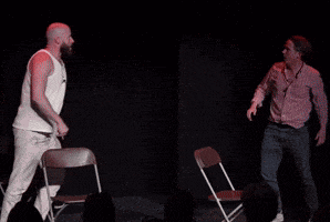 a man in a white tank top is dancing with another man in a red shirt