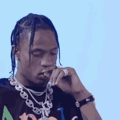 a man with braids is wearing a necklace and a watch and smoking a cigarette .