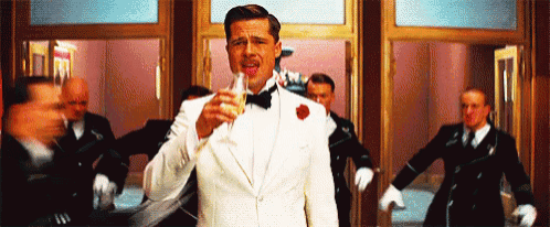 a man in a tuxedo is holding a glass of champagne in front of a group of men .