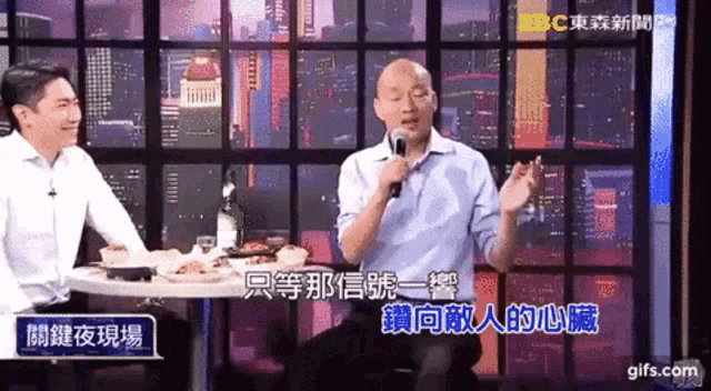 a man is sitting at a table with a microphone in his hand .