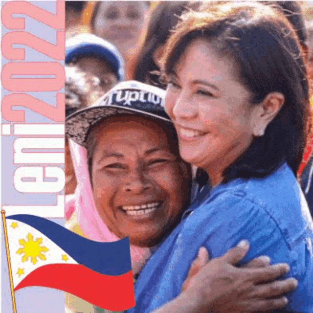 a woman in a blue shirt is hugging an older woman in front of a flag and the year 2022