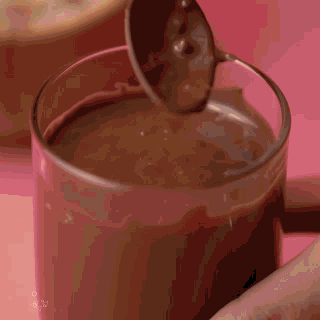 a glass of chocolate sauce is being poured into it with a spoon