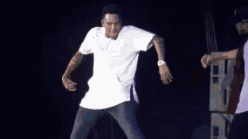 a man in a white shirt is dancing on a stage in a dark room .