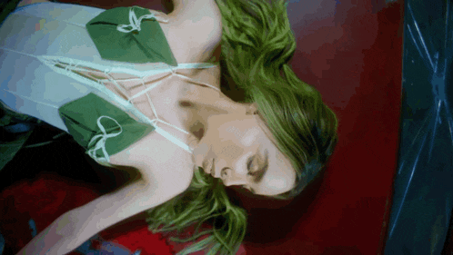 a woman with green hair and a white top is laying on her back