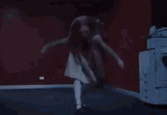 a woman in a white dress is dancing in a dark room in front of a printer .
