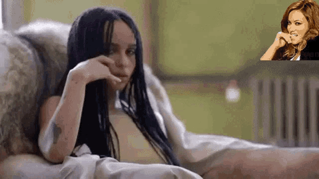 a woman with dreadlocks is laying on a bed with a picture of a woman in the background .