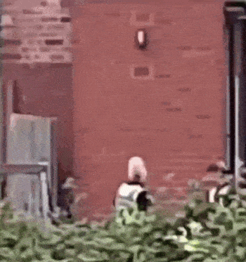 a man in a yellow vest is walking in front of a red brick wall .
