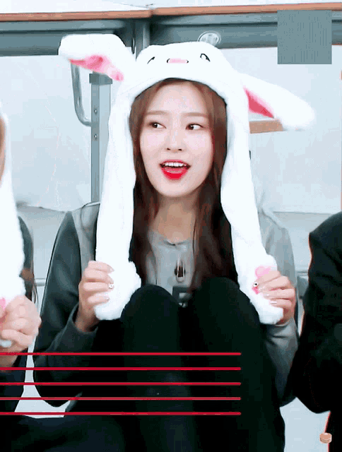 a girl wearing a white bunny hat with pink ears is smiling