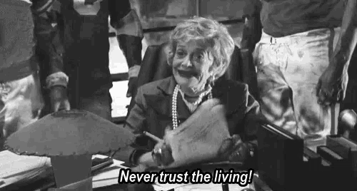 a black and white photo of an elderly woman sitting at a desk holding a piece of paper and a pencil .