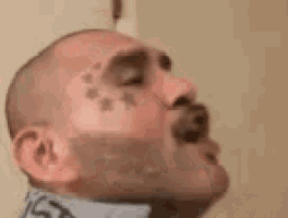a man with a tattoo on his face and neck is yawning .