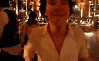 a man in a white shirt is standing in front of a crowd of people in a dark room .