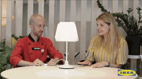 a man and a woman are sitting at a table with an ikea logo on the table