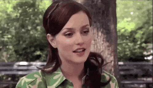 a woman wearing a green shirt and a headband is standing in front of a tree .