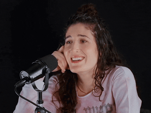 a woman wearing a pink shirt with the word thrasher on it talks into a shure microphone
