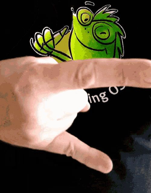 a person 's finger is pointing to a green frog on a black shirt that says ing os