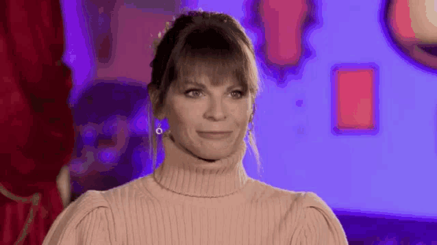 a woman wearing a pink sweater and earrings is smiling and making a face .