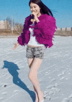 a woman wearing a purple jacket and shorts is standing in the snow .