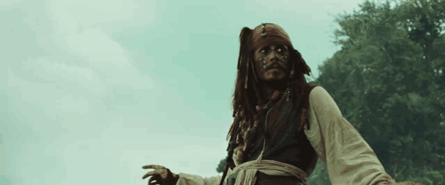 a man with dreadlocks and a bandana on his face stands in front of trees